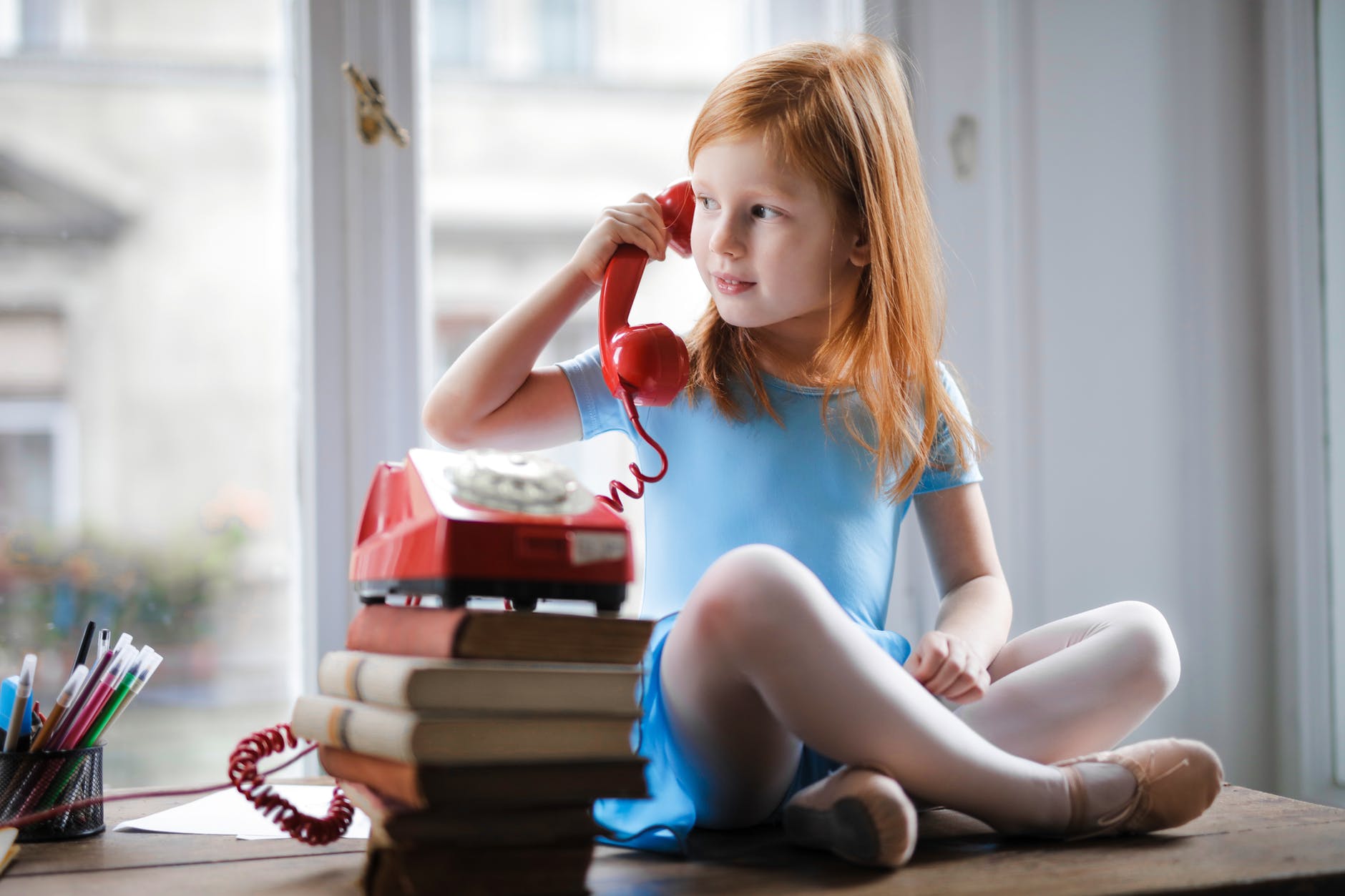 pensive little girl talking on vintage phone while sitting on table in light living room