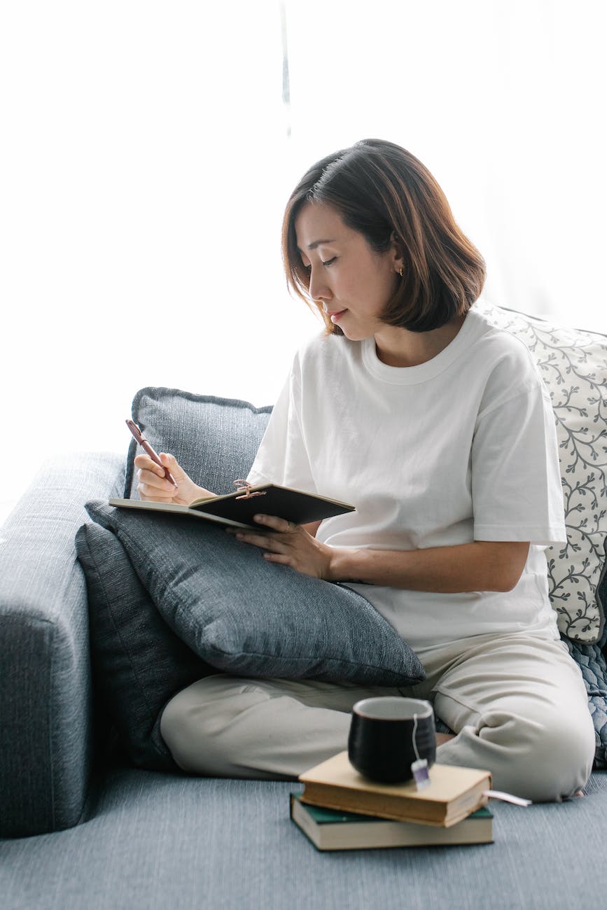 a woman writing in her diary while sitting on a couch